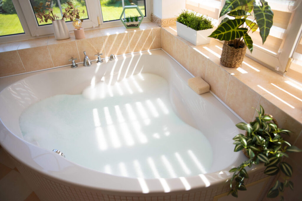Luxurious bathtub filled with bubbles by large windows, bathed in natural light.