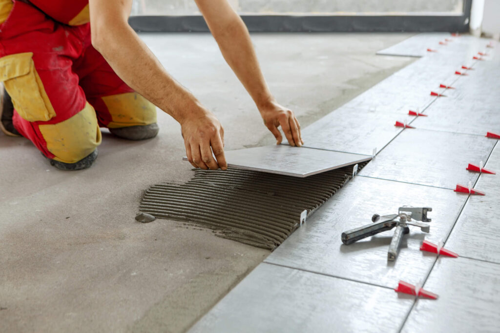 Tiler placing ceramic wall tile in position over adhesive with lash tile leveling system.