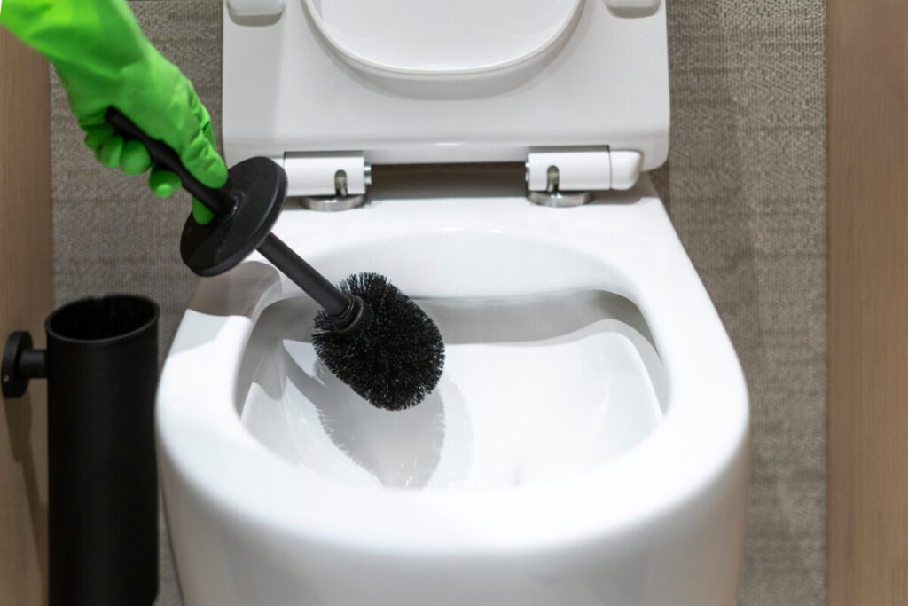 close up of person hand in glove with brush washing toilet bowl in restroom