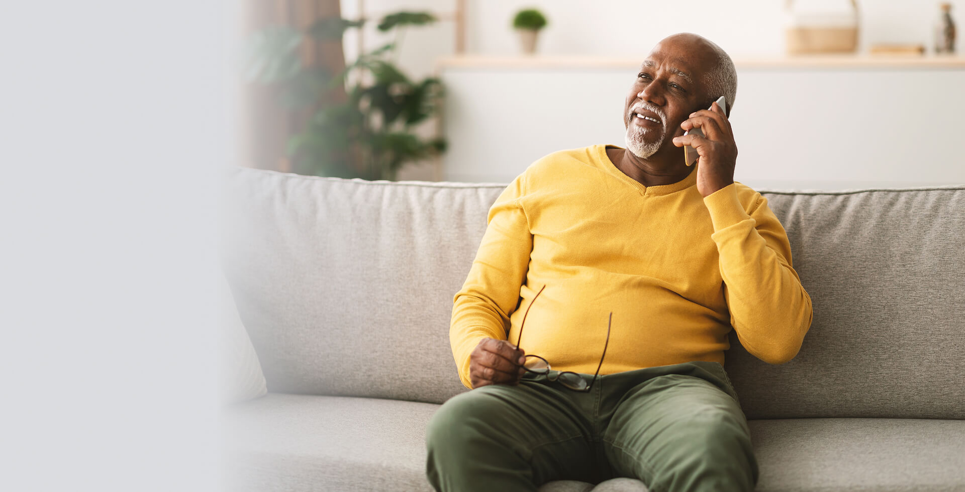 Older man relaxing on a sofa and talking on the phone, smiling in a bright, comfortable living room