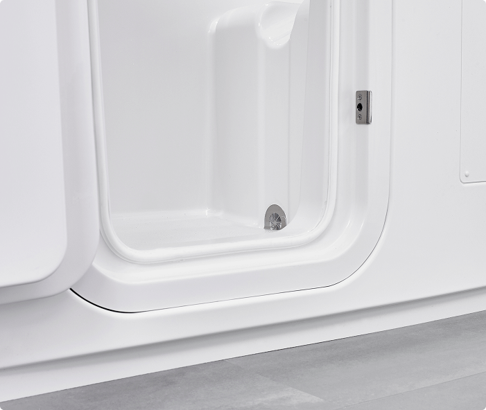 Close-up view of the Grasmere walk-in bathtub’s doorway, showcasing the smooth white interior, watertight door seal, built-in seat, and chrome drain on a tiled bathroom floor. The door is slightly ajar, revealing the secure locking mechanism on the side.