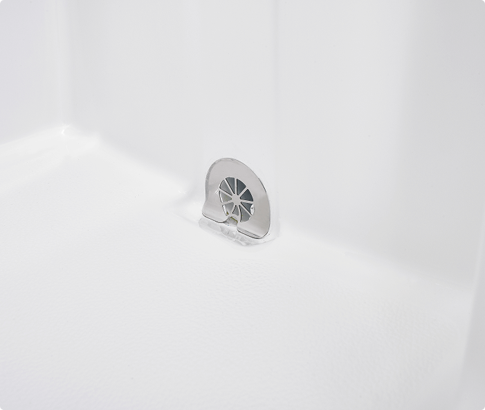 Close-up image of a drain cover inside a walk-in bathtub, set against a clean white textured surface. The drain cover is metallic with a petal-like design for water flow, ensuring safe and efficient drainage in the bathing area.
