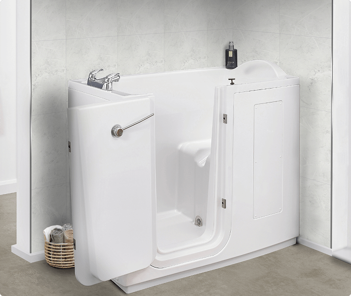 White walk-in bathtub named Grasmere installed in a bathroom corner. The tub features a side-opening door with a secure locking mechanism, chrome taps, and a sleek modern design. The background shows light marble walls, a window with blinds, and a cozy chair nearby.