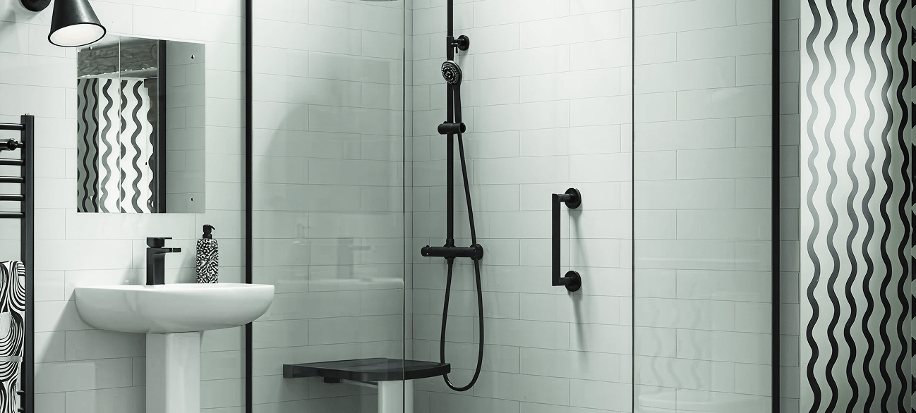 Walk-in shower with black wall-mounted seat, vertical and horizontal grab bars, and handheld shower. Pedestal sink nearby.