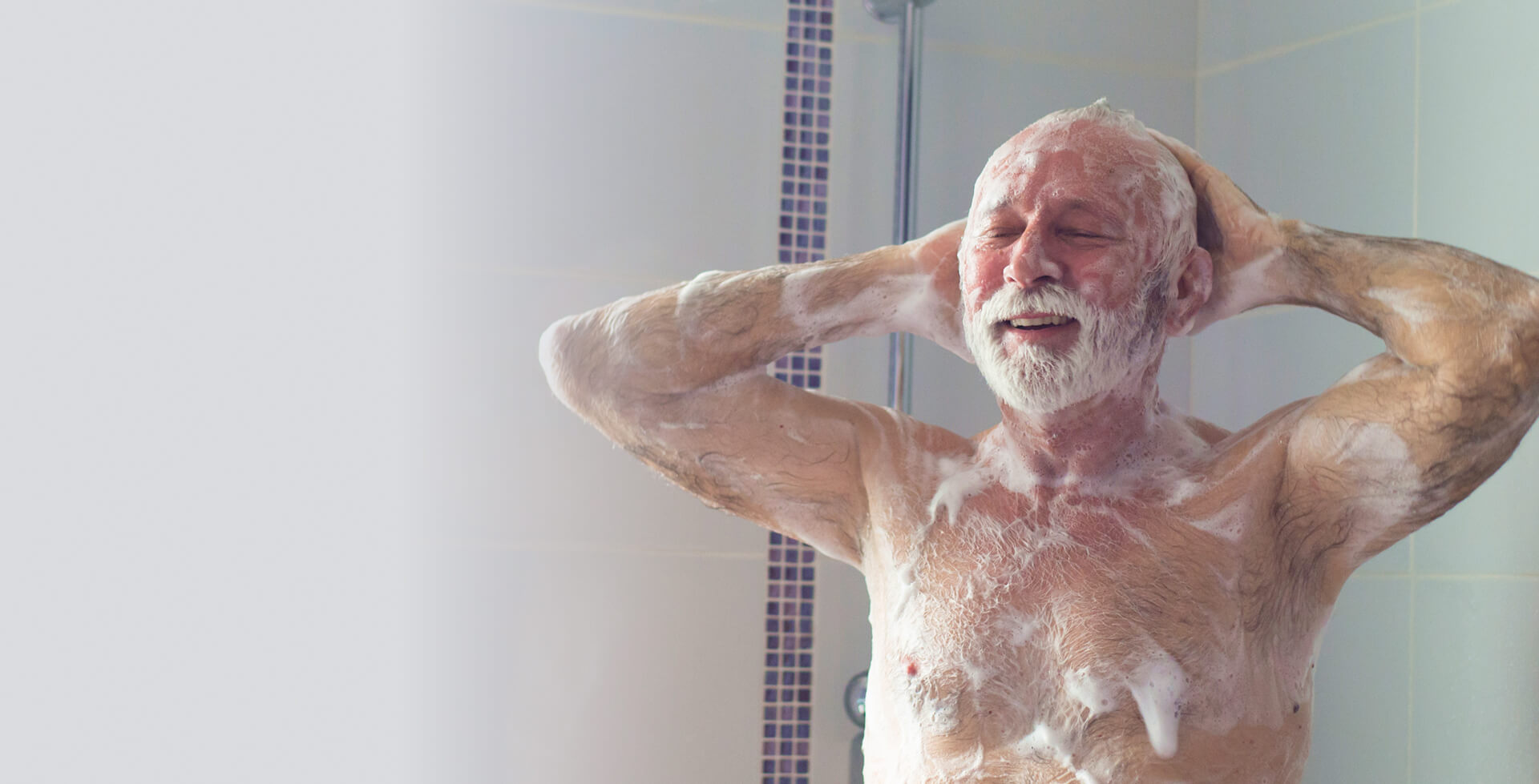 Older man enjoying a shower, smiling with eyes closed and lathered in soap under running water