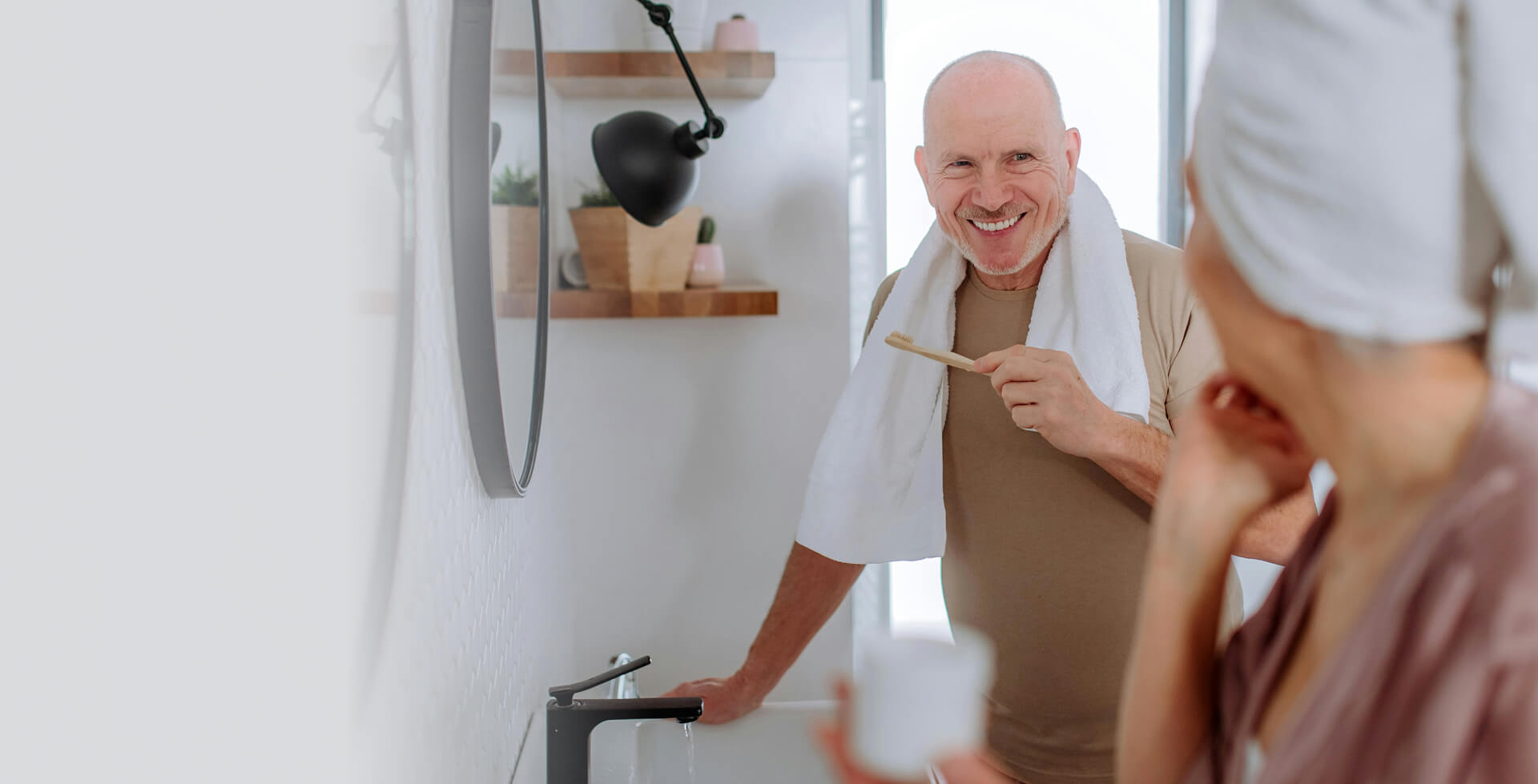 Man smiling with a toothbrush in hand, chatting with a woman in the bathroom