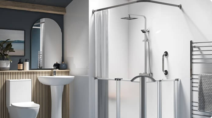 Modern white bathroom with a glass shower enclosure featuring a sliding door and wall-mounted shower system, including a grab bar and a rain shower head. Adjacent is a white toilet and pedestal sink, a large oval mirror with wooden frame, and a vertical towel radiator with a gray towel. The back wall is decorated with vertical wooden slats and plants on the counter.