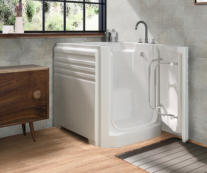 The Earlswood walk-in bath with outward-opening door, upright seat and chrome fixtures, shown in a tiled bathroom with wood-effect floor and mid-century cabinet.