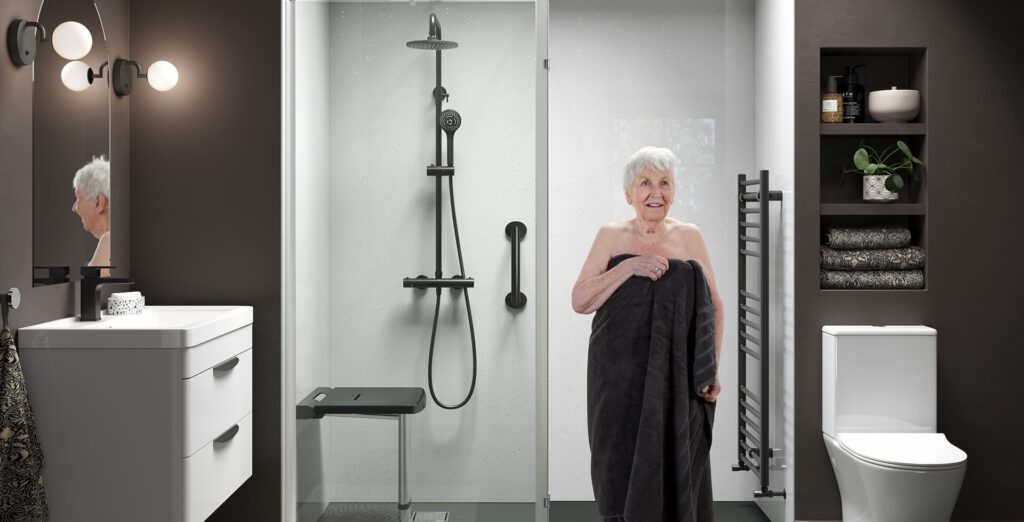 Older woman stepping out of a walk-in shower with a towel, in a modern accessible bathroom with dark walls and grab rails