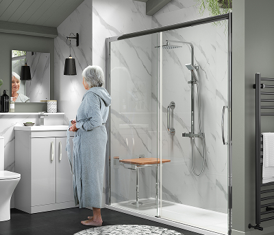 Contemporary bathroom with a Richmond sliding door shower, featuring a fold-down seat and grab rails, beside a woman in a robe standing at the sink.