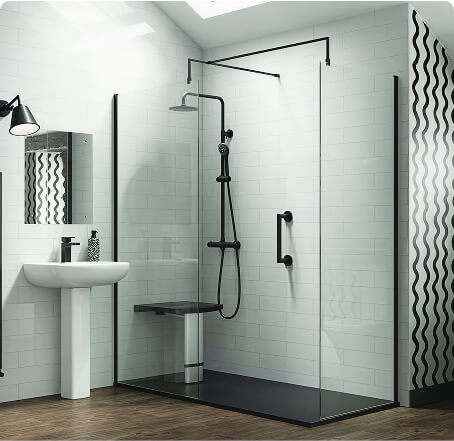 Modern accessible wet room style shower with black fixtures, glass screen, foldable seat, black grab handle, white tiled walls, pedestal sink, black tap, wall-mounted mirror, and wood-effect floor.