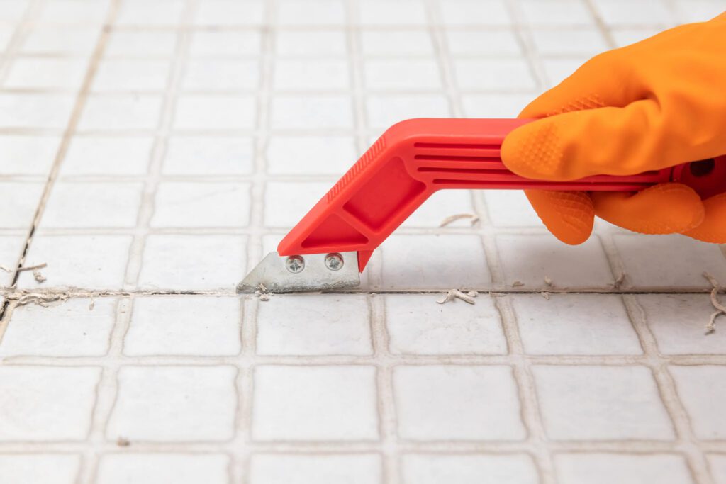 Grout being scraped from between tiles with knife.