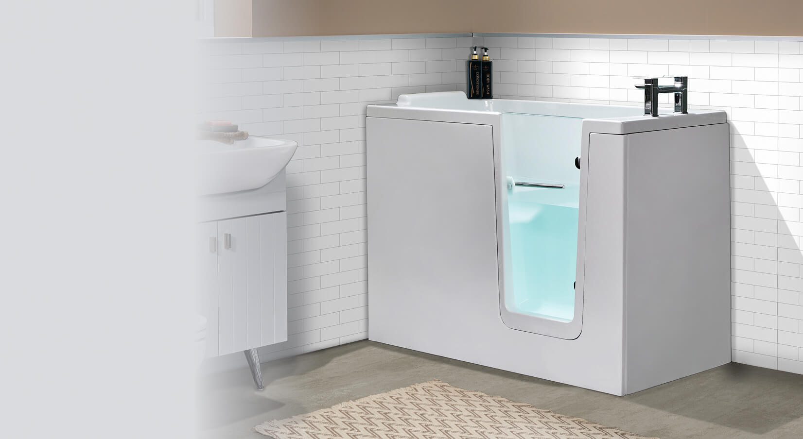 Image showing the Hampton Elite walk-in bath in a bright bathroom with white tiled walls and a beige floor. The bath features a white exterior, a glass door, and a built-in seat inside. The door opens inward, providing easy access. Chrome taps are mounted on the top edge of the bath. The bath is filled with water, giving a clear view through the glass door.